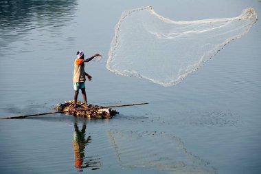 Sangli, Maharashtra, Hindistan 'da Krishna nehrinde balık yakalamak için balıkçı ağlarını attığı derme çatma bir tekneyle Haripur köyünden bir balıkçı.
