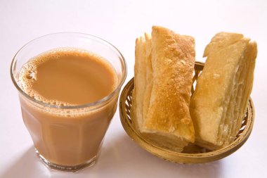 Toprak çaydanlıkta çay ve beyaz arka planda kamış sepetinde khari bisküvileri.