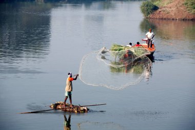 Sangli, Maharashtra, Hindistan 'da Krishna nehrinde balık yakalamak için balıkçı ağlarını attığı derme çatma bir tekneyle Haripur köyünden bir balıkçı.