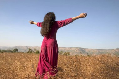 Girl dressed in maroon robe ;  dancing under open sky with joy ;  Osho devotee ;  nature ;  Mystic village ;  Pune ;  Maharashtra  ; India  clipart