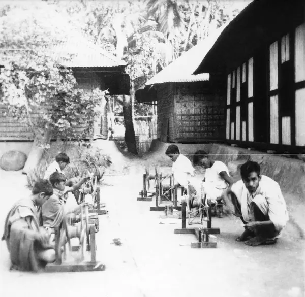 Stock image A group of young men sitting in front of huts and spinning on big size charkhas spinning wheels in the riot effected area at Noakhali East Bengal, November 1946, India   