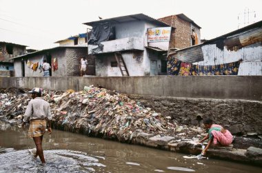 A woman washing cloth in dirty water along a canal dumped with garbage in a slum in Bombay now Mumbai, Maharashtra, India  clipart