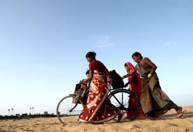 Women walking and carrying lad on cycle, Garwa and Latehar, Jharkhand, India  clipart