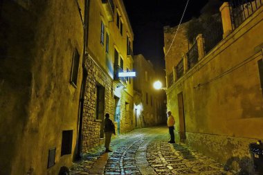 Dar sokakta gece ayakta duran kadın ve erkek, Erice, Trapani, Sicilya, İtalya, Avrupa  