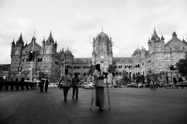 Man with crutches crossing road, Victoria Terminus, VT, Chhatrapati Shivaji Maharaj Terminus, CST, UNESCO World Heritage Site, Bori Bunder, Bombay, Mumbai, Maharashtra, India, Asia clipart