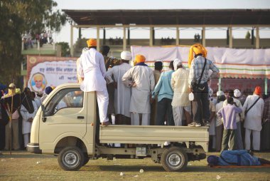 Sikh tutkunları temponun tepesinde durmuş Nihang ve Sih savaşçılarının dublörlüklerini izliyorlar, 300 yıldır süregelen kültürel etkinlikler sırasında Khalsa Spor sahasında Sih Guru Granth Sahib 'in kutlanması, Nanded, Maharashtra, Hindistan 