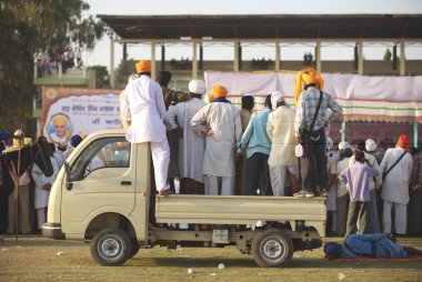 Sikh devotees standing on top of tempo watching stunts of Nihangs or Sikh warrior, during cultural events for 300th years celebrations of Consecration of perpetual Sikh Guru Granth Sahib at Khalsa Sports ground, Nanded, Maharashtra, India  clipart