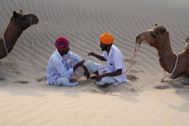 Two men with camels resting in desert, Khuri, Jaisalmer, Rajasthan, India  clipart
