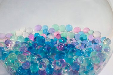 Beyaz arka planda büyük yuvarlak cam kavanozda renkli jel toplar.