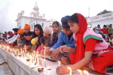 Altın Tapınak 'ın narları üzerinde mum yakan çocuklar; Harimandir Granth Sahib olarak da bilinir; Amritsar' da Sikhs 'in kutsal ibadethanesi; Punjab; Hindistan; Birinci Sih Guru Sri Guru Dev ji du' nun doğum yıldönümü vesilesiyle