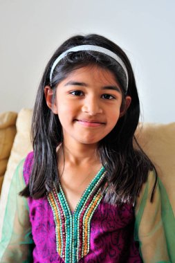 Evdeki kanepede otururken gülümseyen tatlı küçük kız.