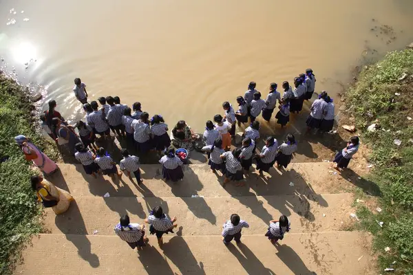 Top view, school girls wearing uniform of blue shirt with white cheques and dark blue skirt standing on Crocodile Ghat on bank of river Poorna at Adi Shankarachaya temple, Kaldi, Kerala, India 