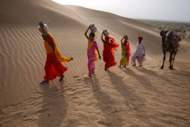Kadınlar çölde deve adamla, Jaisalmer 'le, Rajasthan' la, Hindistan 'la yürüyor.