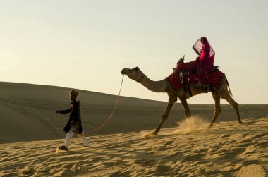 Üzerinde kadın olan Deve Sürükleyen Adam Kum Kumulu Jaisalmer Rajasthan Hindistan Asya 