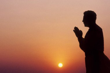 Erkek silueti gün batımında dua ediyor.  