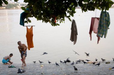 Human activities on bank of river Hooghly, people bathing drying cloths hanging on banyan tree, Calcutta now Kolkata, West Bengal, India  clipart