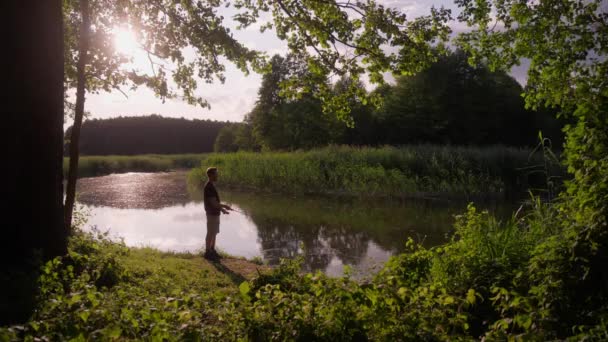 Ψαράς Στέκεται Στην Όχθη Ενός Γραφικού Ποταμού Στο Ηλιοβασίλεμα Και — Αρχείο Βίντεο