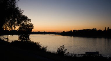 Gün batımında banklı ve ağaçlı bir göl.