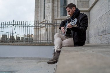 Boş bir meydanda gitar çalan sakallı bir müzisyenin arka planı..