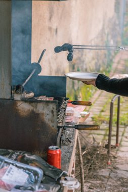 Beyaz bir kadının kolu boş bir tabağa koymak için barbeküden maşayla et çıkartıyor. Dikey.