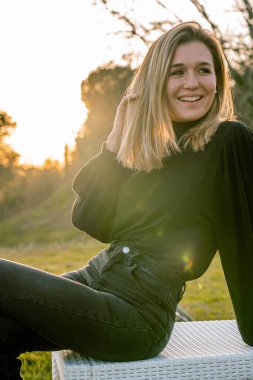 Siyah giyinmiş genç sarışın kadın altın saatinde gülümseyerek yan tarafına bakıyor. Dikey.