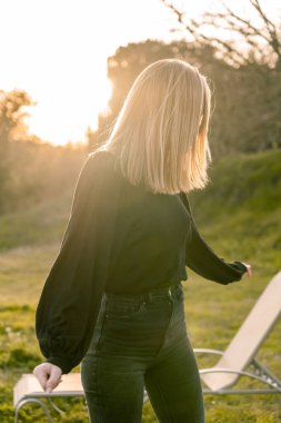 Tanımlanamayan sarışın manken. Yüzü saçlarıyla kaplı. Güneş batarken kollarını açıyor..