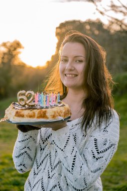 Beyaz kazaklı genç kadın yanlış mumlu bir doğum günü pastası tutuyor..