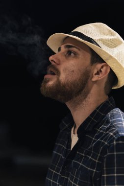 Siyah arka planda ağzından duman çıkaran bir adamın dikey portresi. Boşluğu kopyala.