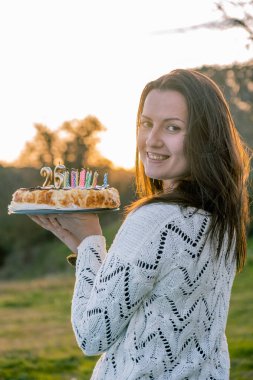 Beyaz kazaklı, 26. yaş gününde doğum günü pastası tutan doğal bir genç kadın. Boşluğu kopyala.