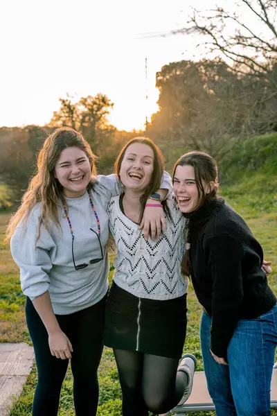 Portrait of three young women laughing loudly in a park at sunset. Friendship concept.