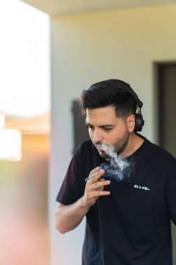 Siyah elbiseli genç adam esrar içerken kulaklıkla müzik dinliyor..