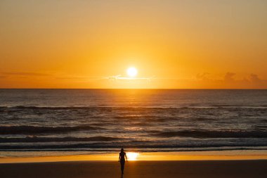 Gün batımında sahilde yalnız ve kendine güvenen bir kadının silueti..