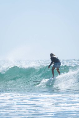 Kıdemli yetişkin, kısa mayosuyla şehir plajında dalgalarda sörf yapıyor..