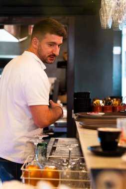 Beyaz polo tişörtlü garson bir restoranın arkasında çalışıyor. Dikey.