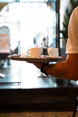 Tepsisi kahveyle dolu barmen tek eliyle tutuyor. Dikey.