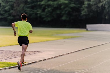 Sporcu atletizm pistinde koşarken büyük adımlar atıyor. Boşluğu kopyala.