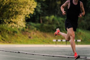 Siyah elbiseli ve turuncu ayakkabılı tanınmayan bir sporcu pistte koşuyor..