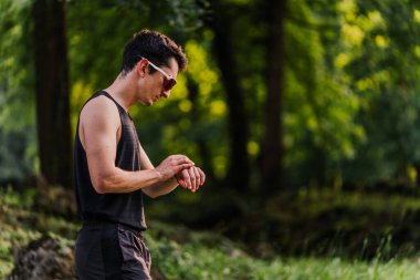 Athlete wearing sunglasses looking at his smart watch during a training session. clipart