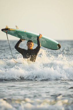 Mutlu genç adam sörf tahtasını başının üstüne kaldırıyor..
