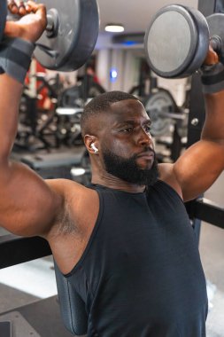 Spor salonunda dambıllarla askeri basın toplantısı düzenleyen siyah bir adam..