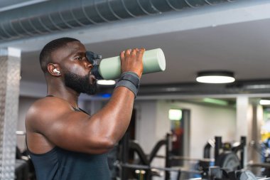 Spor salonunda egzersiz yaparken su içen siyahi bir adam..