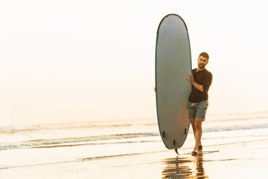 Sahilde sörf tahtası olan bir erkek sörfçü. Boşluğu kopyala.