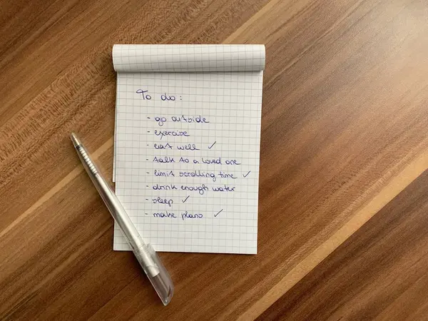 Handwritten to do list with self care points for mental and physical health on a checkered notepad in cursive letters