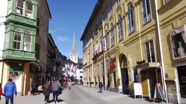 Bad Ischl, Yukarı Avusturya, Avusturya, 09 Mart 2024: Avrupa Kültür Başkenti Bad Ischl, Avusturya 'da güneşli bir baharda eski binalarda dükkanları olan kalabalık yaya bölgesi. Arka planda kilise ve bayraklar.