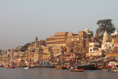 Varanasi, Hindistan - 13 Mart 2019: Varanasi 'deki Ganj nehrinin kıyısındaki Munshi Ghat' ta günlük yaşam birçok renkli tekne ve eski binalarla birlikte. yumuşak ışık. Bir tekneden görüntü.