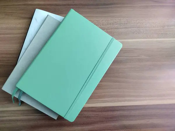 Beyaz mermer, yeşil ve gri defterler koyu ahşap masaya istiflenmiş. Ahşap arka planda izole edilmiş kurşun günlük planlayıcıları. Yeni Yıl Kararları veya Organizasyonu Konsepti.