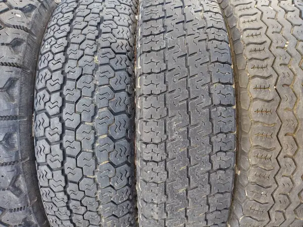 Close up of four worn black tires, joined together, with four different tire treads or profiles. Tread of tire refers to the rubber on its circumference that makes contact with road or ground.  Pattern of grooves molded into rubber