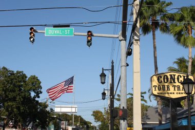 Key West, Florida, ABD - 12 Şubat 2020: kavşakta Duval caddesi yazan tabela, büyük Amerikan bayrağı sallama, fenerler ve trafik ışıkları. Deniz kabuğu turu tren karşılama merkezinin büyük işareti.. 