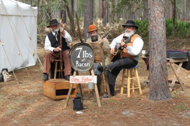 Olustee, Florida, USA - February 16, 2020: Band 7 lbs of bacon perfoms at Olustee Re-enactment in Florida 2020. Musicians playing authentical music in traditional clothing. Southern. Civil war era. Three musicians with hats and beards. Nostalgia clipart