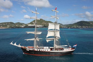 Sint Maarten, Netherlands - November 26, 2016: high angle shot of Mercedes, a dutch briggs ship. Two masts sailing ship at the shore of caribbean island Sint Maarten sailing away. Set sail. Sailboat in front of a tropical island and turquoise sea. clipart
